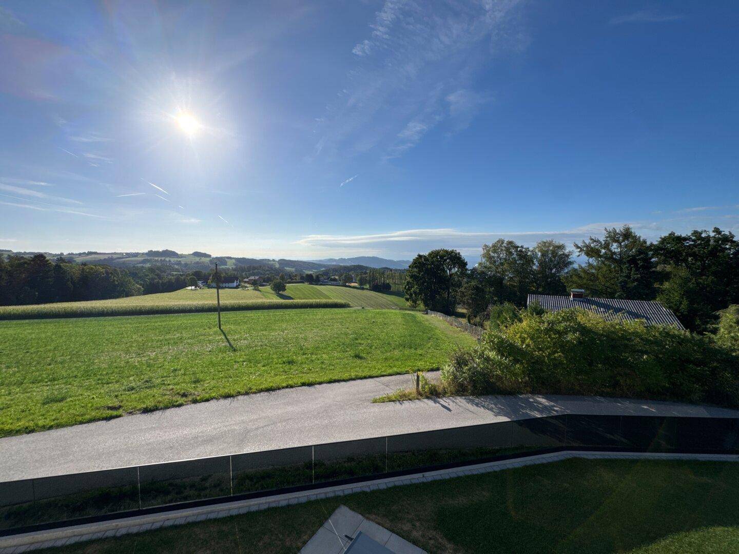 Sonniger Ausblick auf die idyllische Hügellandschaft mit Feldern und Bäumen unter klarem Himmel.
