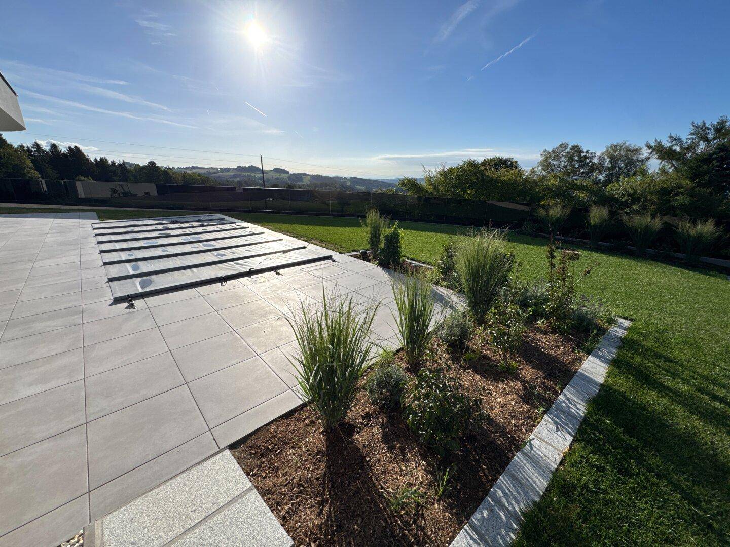 Gepflegter Gartenbereich mit Terrasse, Poolabdeckung und jungen Pflanzenbeeten.