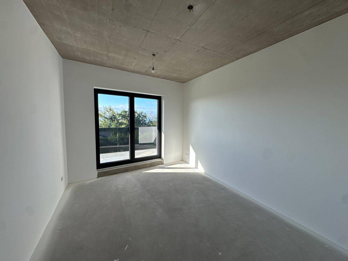 Geräumiges Schlafzimmer im Rohbau mit weißen Wänden und Zugang zu einem Balkon oder einer Terrasse.