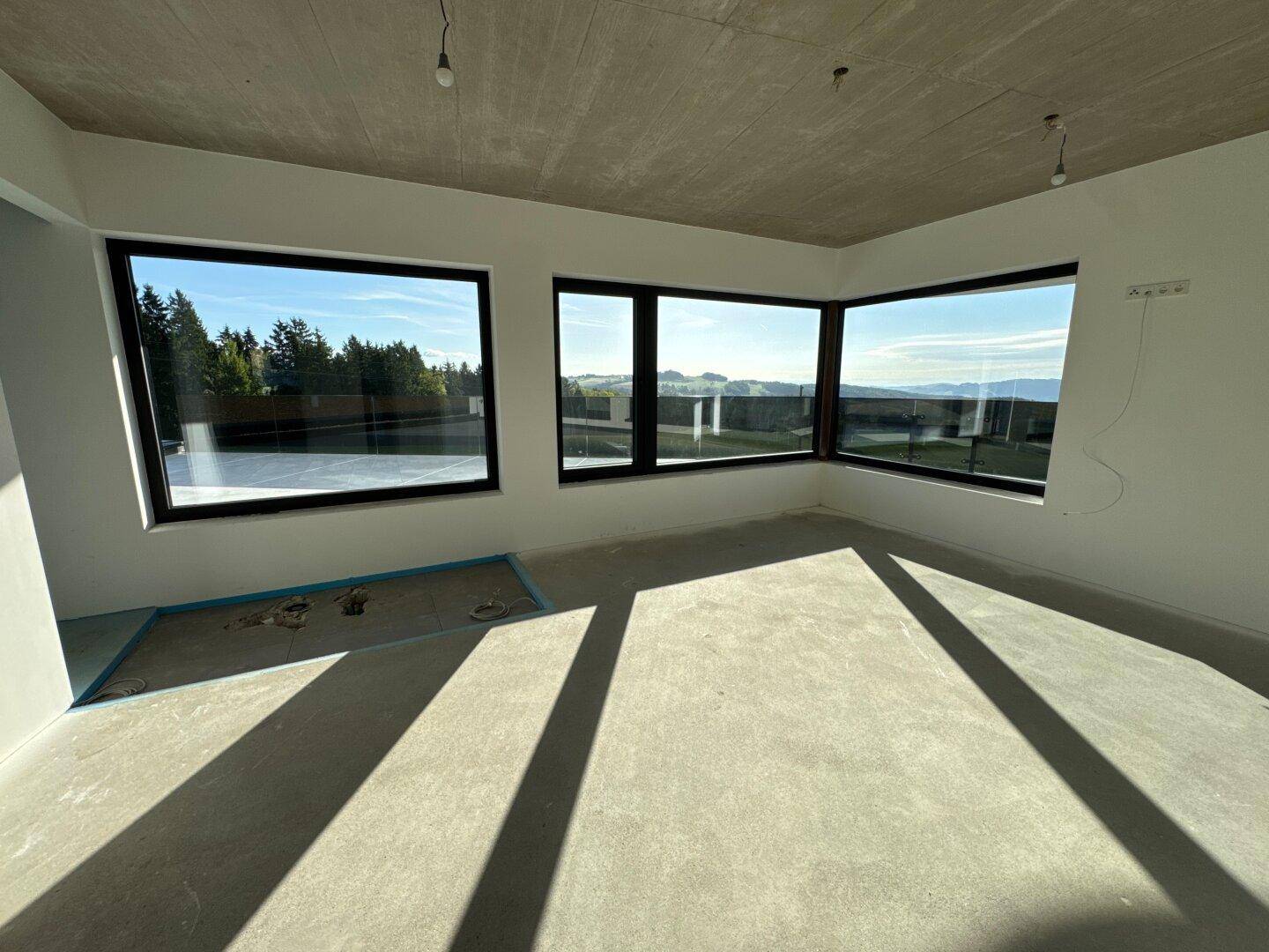 Heller Wohnbereich im Rohbau mit großen Panoramafenstern und weitem Blick über die Landschaft.