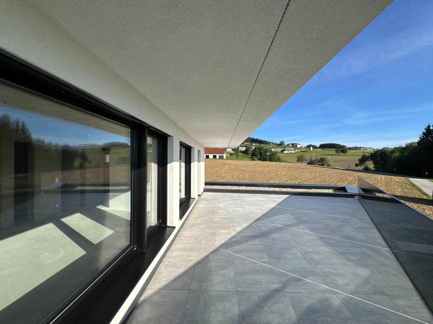 Große, moderne Terrasse mit Fliesenboden und weitem Blick über die ländliche Umgebung.