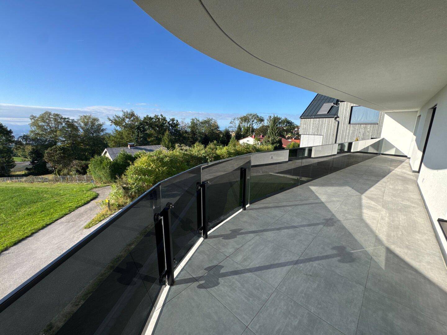 Moderner Balkon mit Glasgeländer und weitem Blick ins Grüne und auf die umliegende Landschaft.