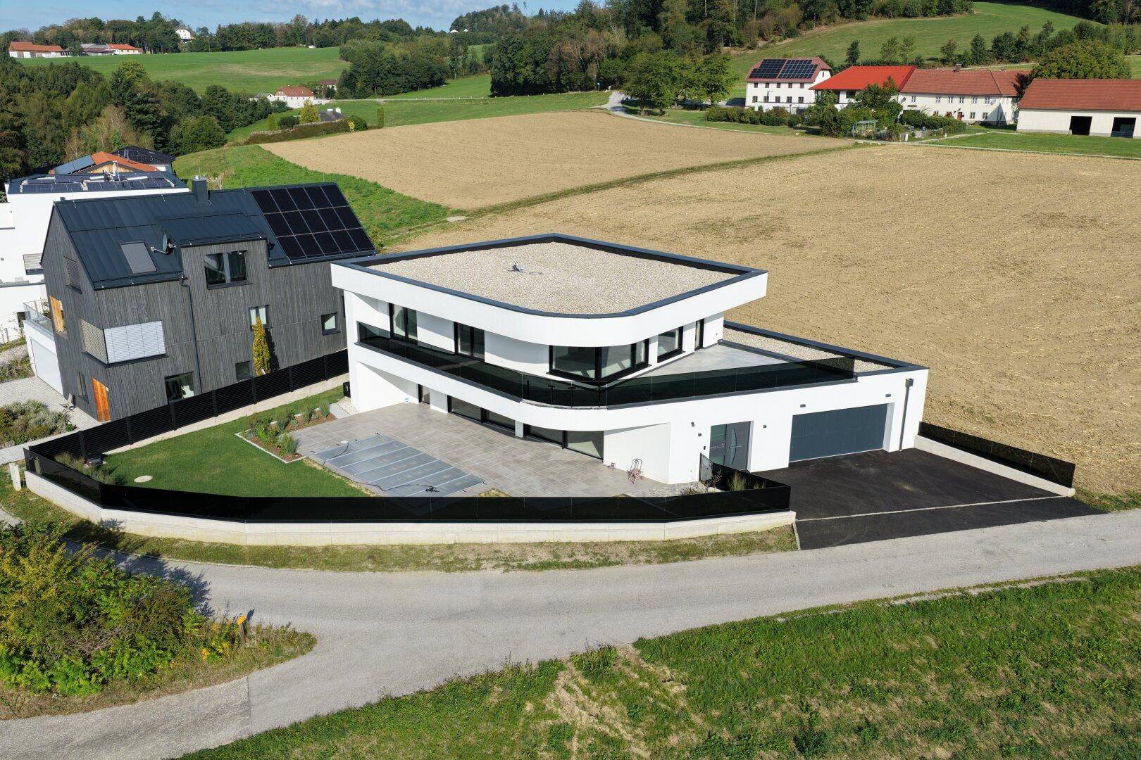 Moderne weiße Villa mit Flachdach, großen Fenstern und integrierter Garage in ländlicher Umgebung.