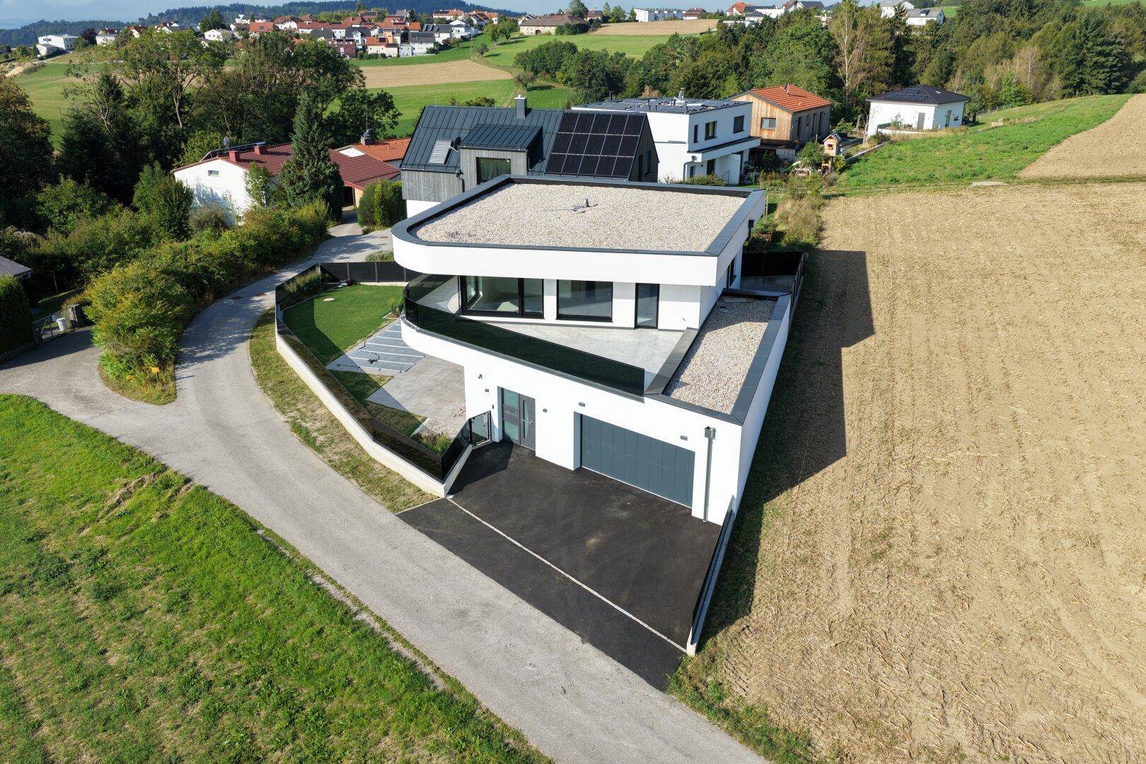 Zeitgenössisches Einfamilienhaus mit Flachdach und Garage, eingebettet in eine ländliche Landschaft.