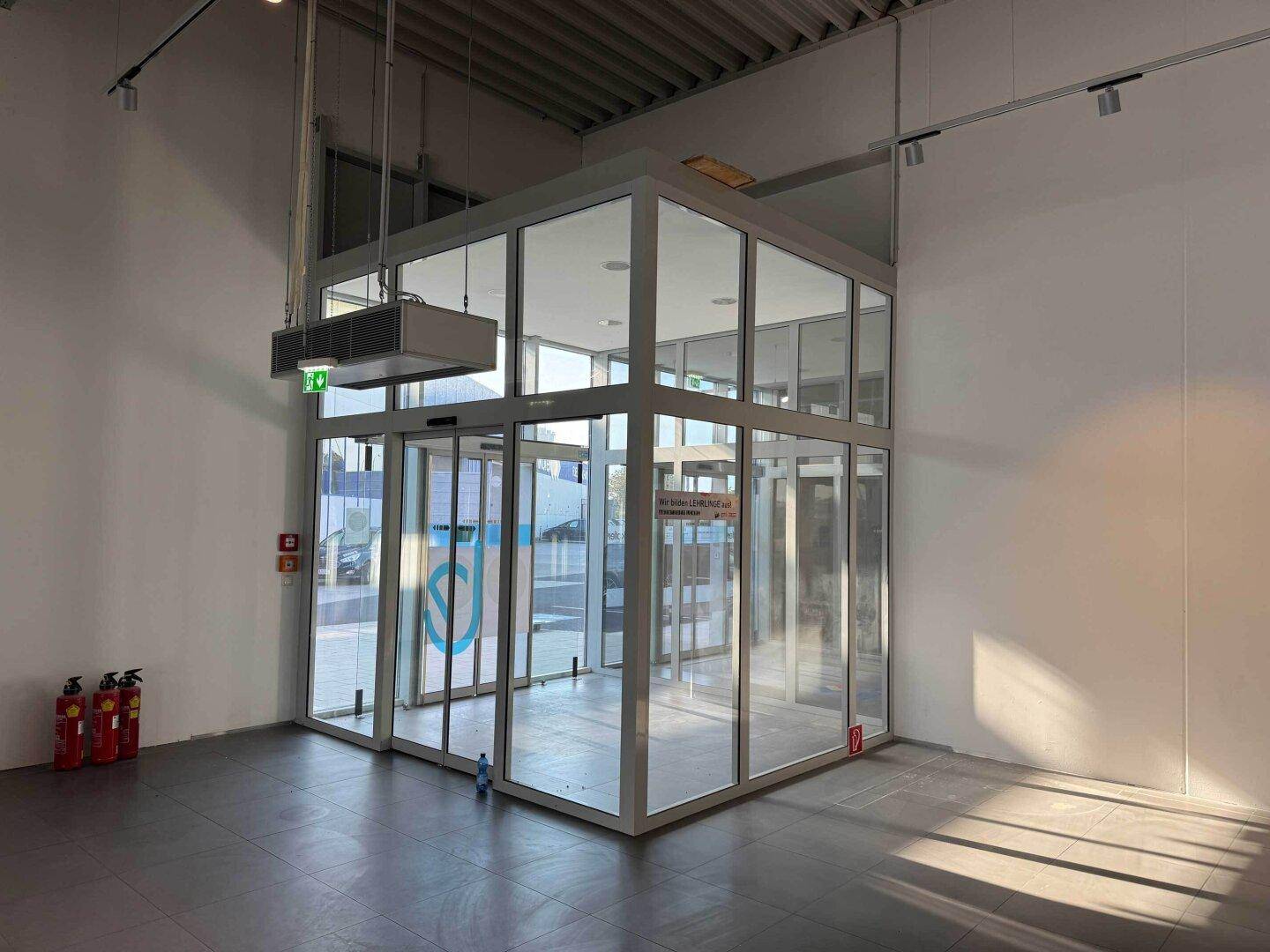 Heller, gläserner Eingangsbereich mit automatischen Türen und viel Tageslicht in einem Gewerbegebäude.