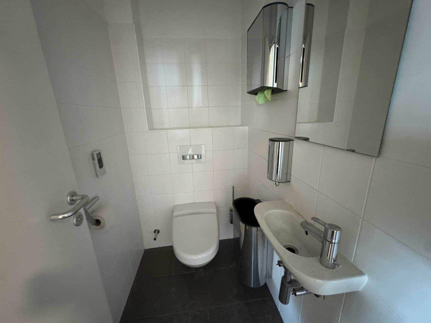Saubere Gästetoilette mit wandhängendem WC, kleinem Waschbecken und Spiegel, hell gefliest.