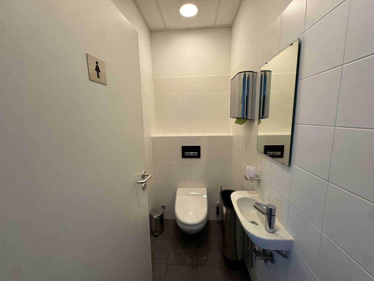Helle Gästetoilette mit wandhängendem WC, Waschbecken und Spiegel, in gutem Zustand.