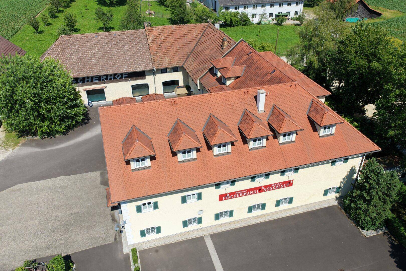 Vogelperspektive des Gebäudes mit rotem Ziegeldach und Gaubenfenstern, umgeben von Natur.