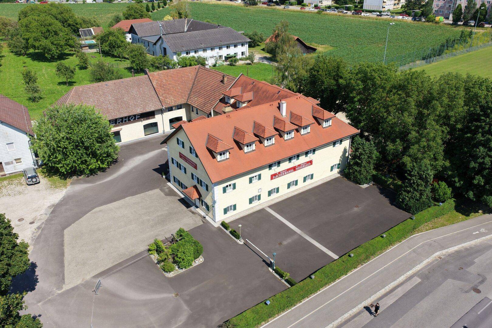 Weitläufige Luftaufnahme des Anwesens mit Parkplätzen und angrenzenden Feldern unter blauem Himmel.