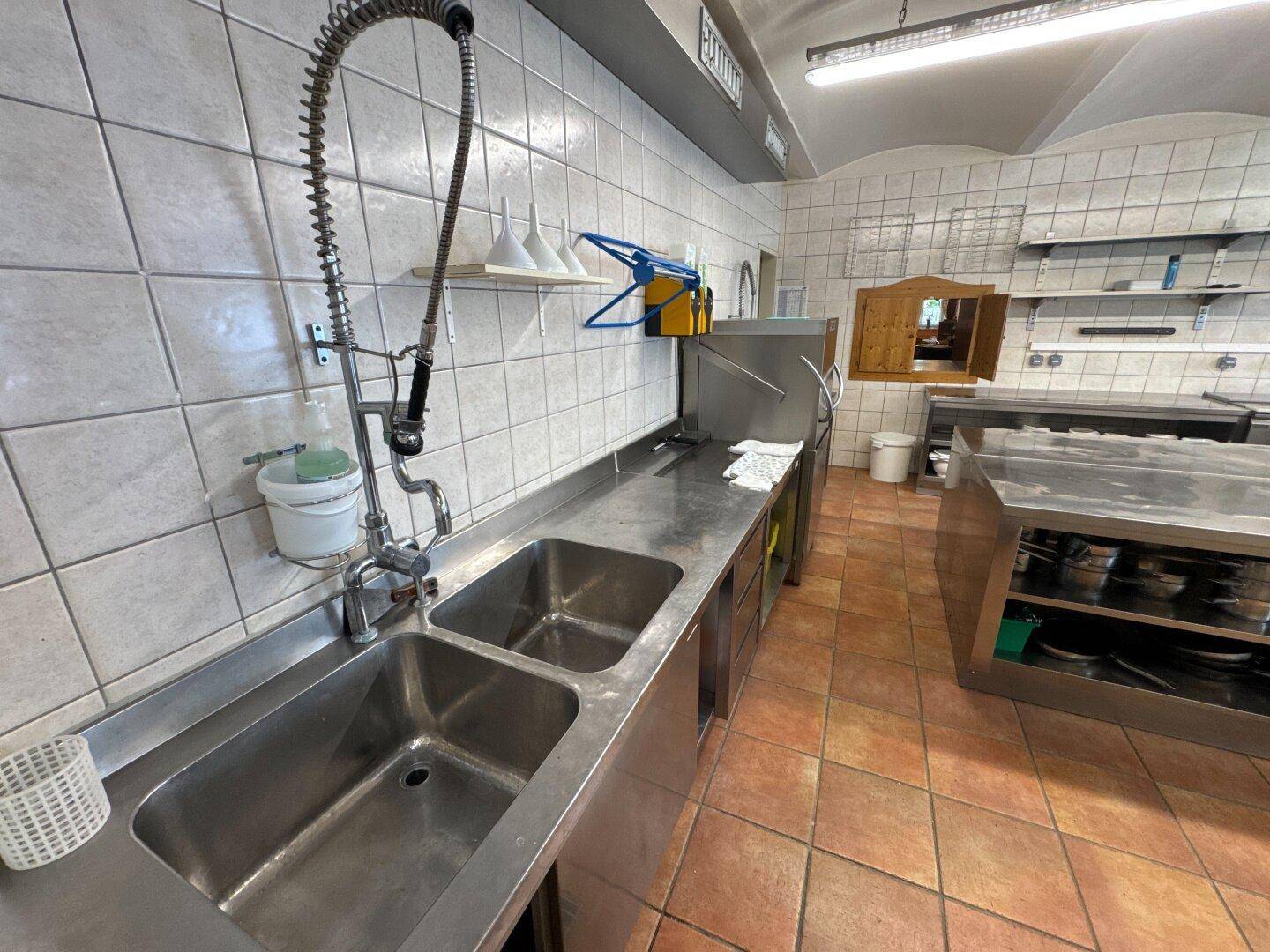 Gewerbliche Spülküche mit Edelstahlbecken, weißen Fliesen und funktionaler Ausstattung.