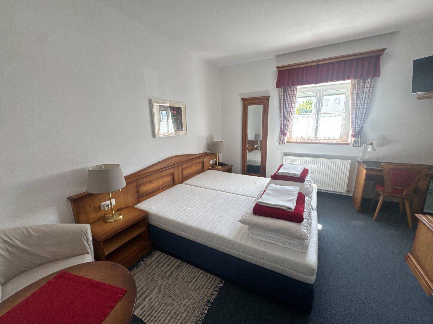 Helles Schlafzimmer mit zwei Einzelbetten, Holzmöbeln und Teppichboden.
