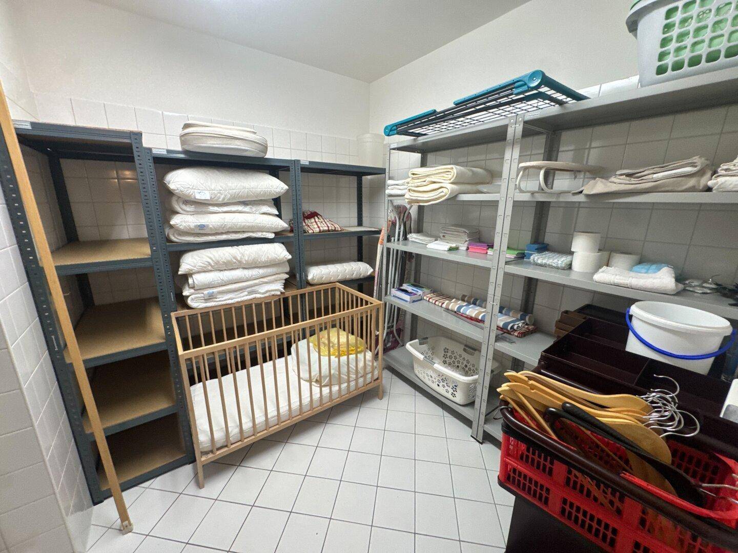 Praktischer Abstellraum mit Regalen für Wäsche und einem Babybett, funktional eingerichtet.