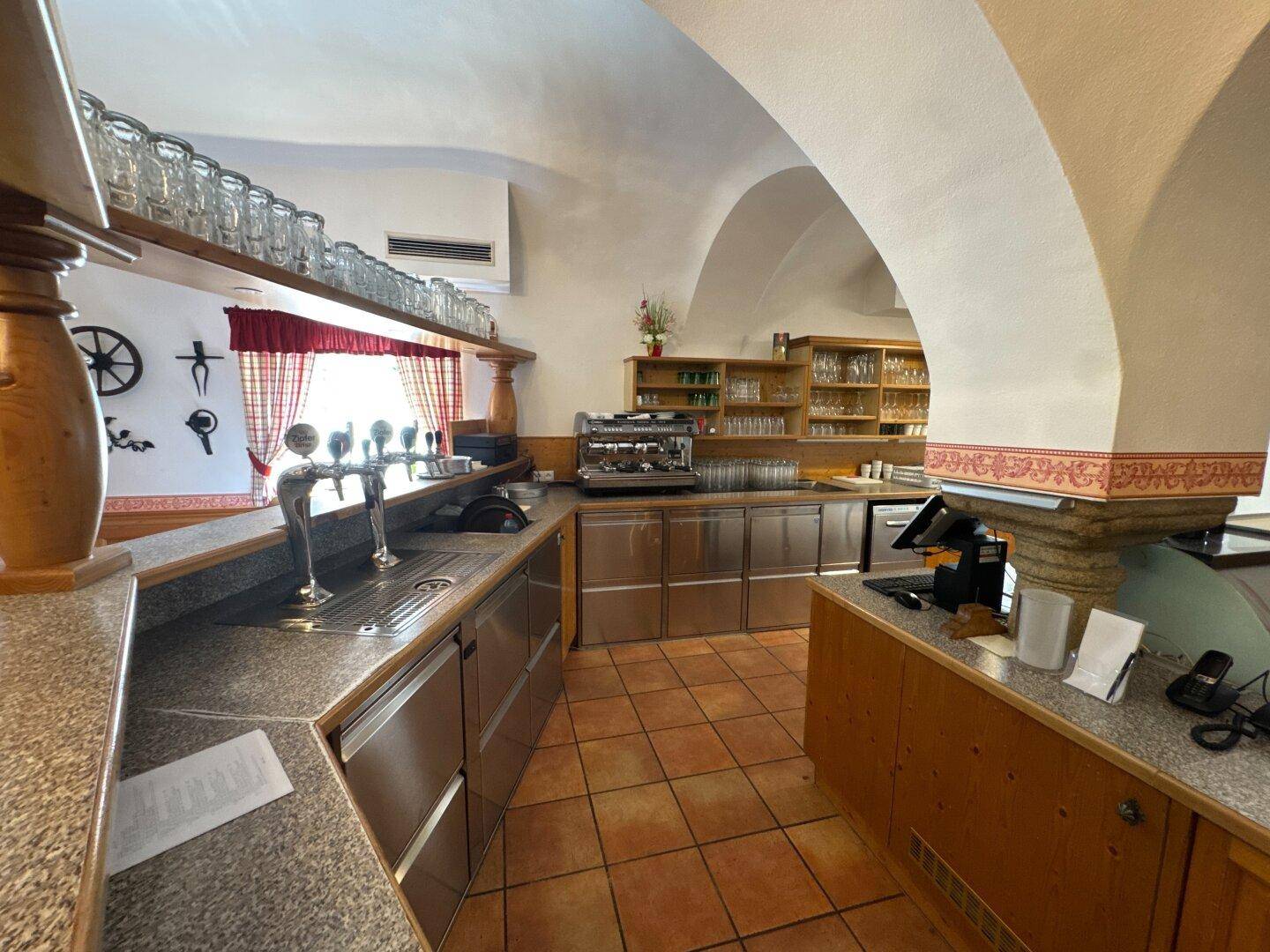 Bar- und Thekenbereich mit Zapfanlage, Kaffeemaschine und vielen Gläsern.
