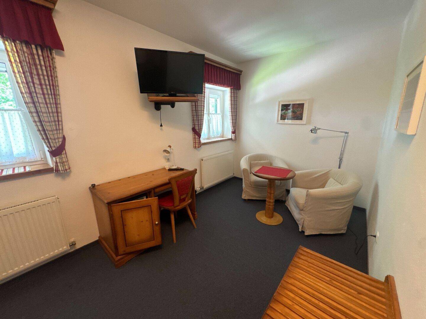 Kleiner Wohnbereich mit zwei Sesseln, Schreibtisch und Fernseher in einem Hotelzimmer.