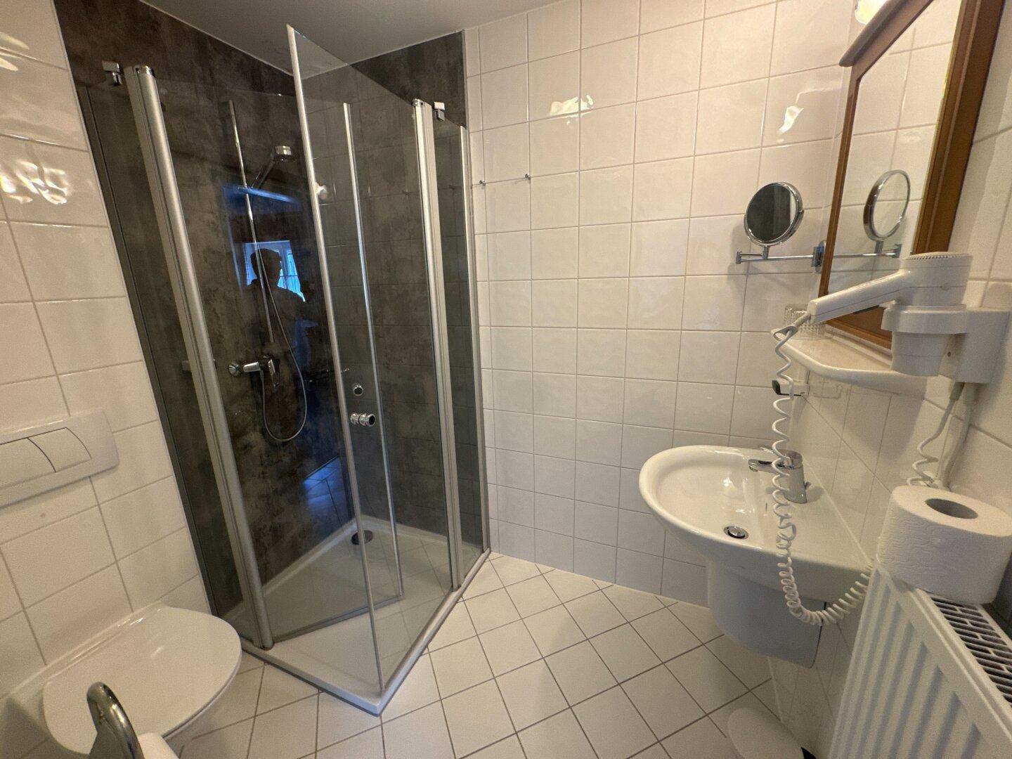 Modernes Badezimmer mit Duschkabine, Waschbecken und weißen Fliesen.