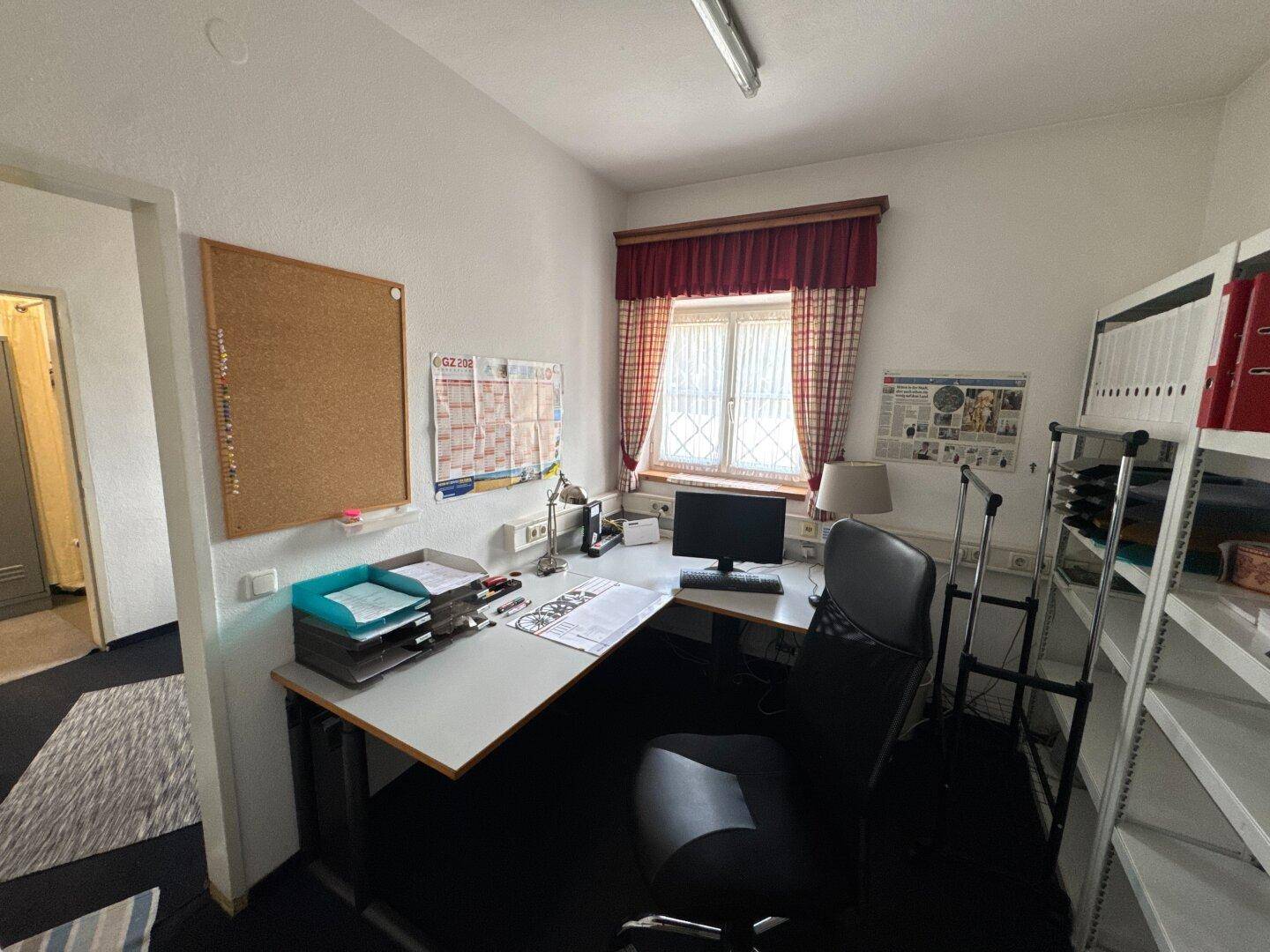Funktionales Büro mit Schreibtisch, Computer und Regalen, gut beleuchtet.