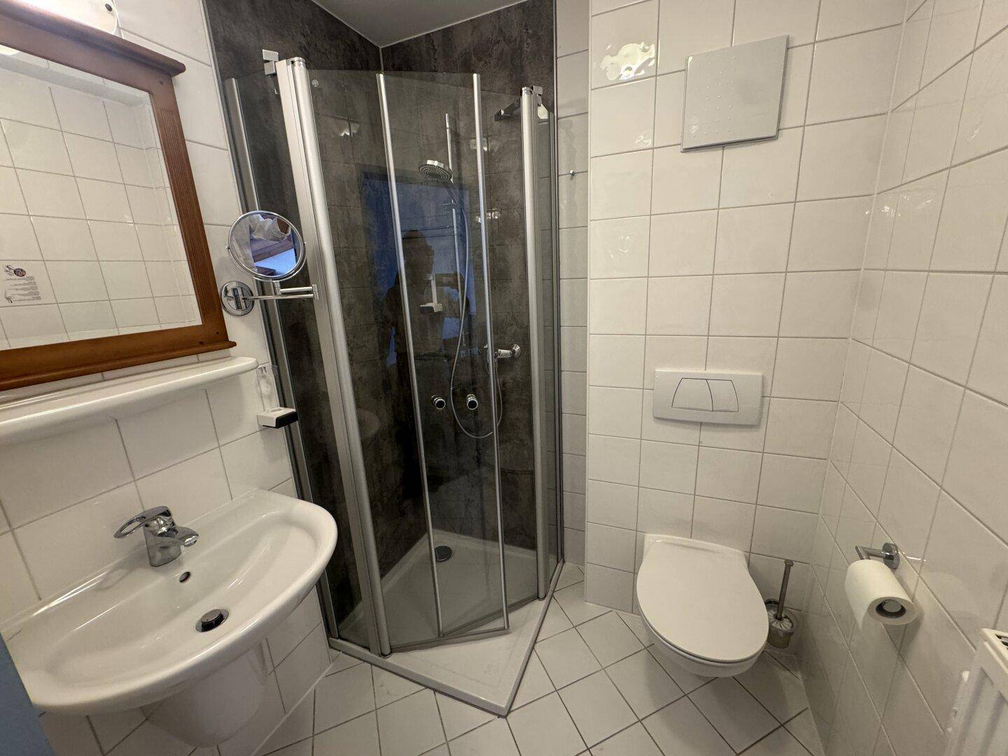 Helles Badezimmer mit Duschkabine, Waschbecken und weißen Wandfliesen.