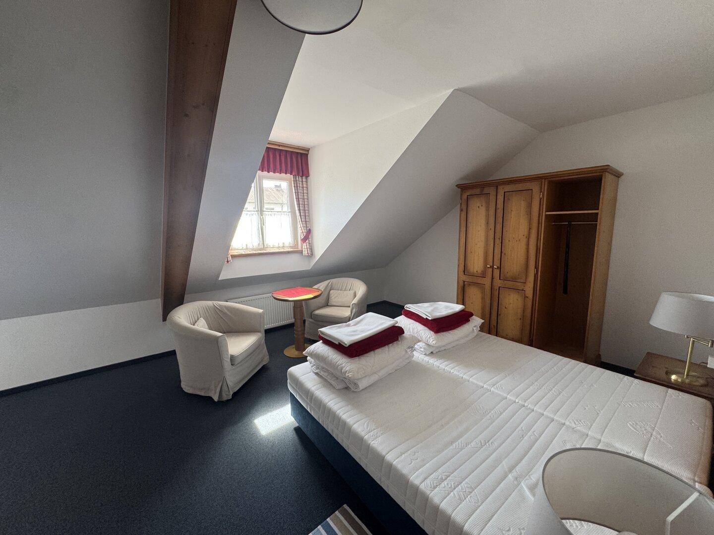 Helles Dachzimmer mit zwei Einzelbetten, Holzschrank und schrägen Wänden.