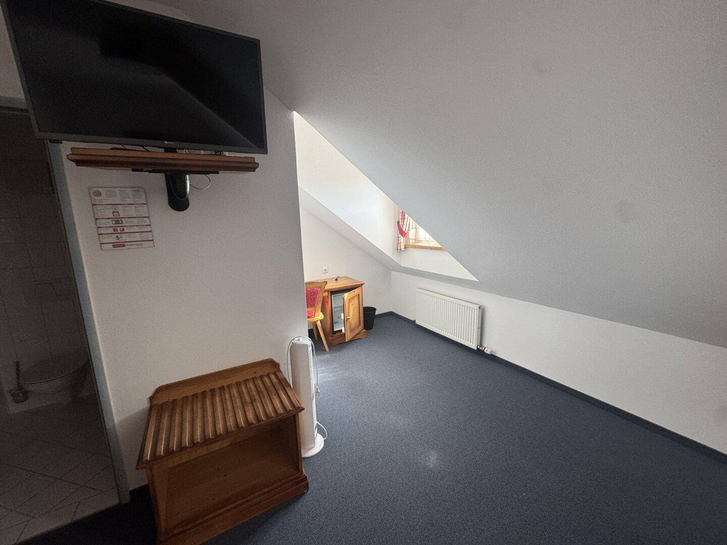 Dachzimmer mit Fernseher, Schreibtisch und schrägen Wänden, funktional eingerichtet.