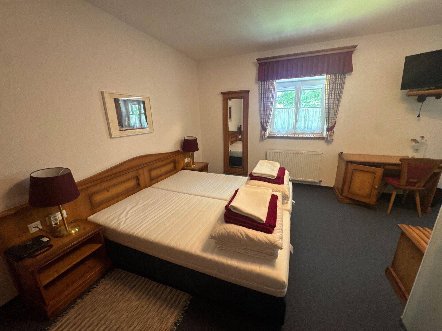 Gemütliches Schlafzimmer mit zwei Einzelbetten, Holzmöbeln und einem kleinen Fenster mit Vorhängen.