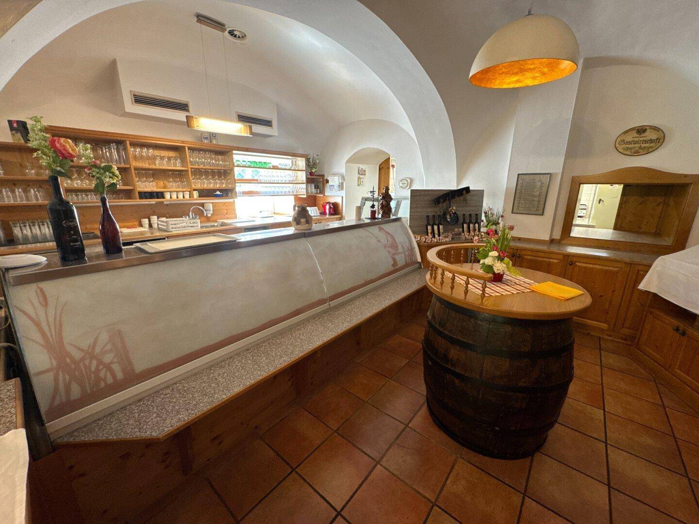 Bar-Bereich mit Theke, Glasregalen und einem dekorativen Weinfass unter einer gewölbten Decke.