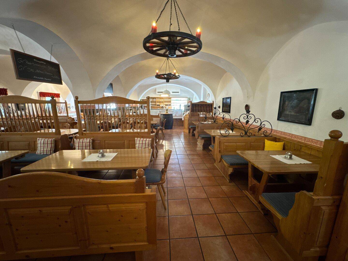 Weiterer Blick in den traditionellen Speisesaal mit Holzbänken, Tischen und gewölbter Decke.