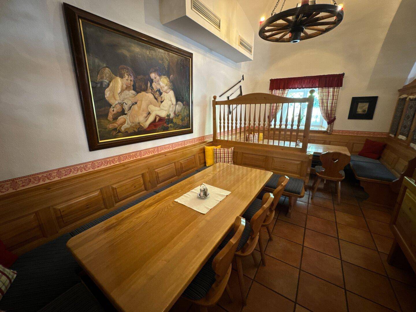 Essbereich mit langem Holztisch, Bänken und einem großen Gemälde an der Wand unter gewölbter Decke.