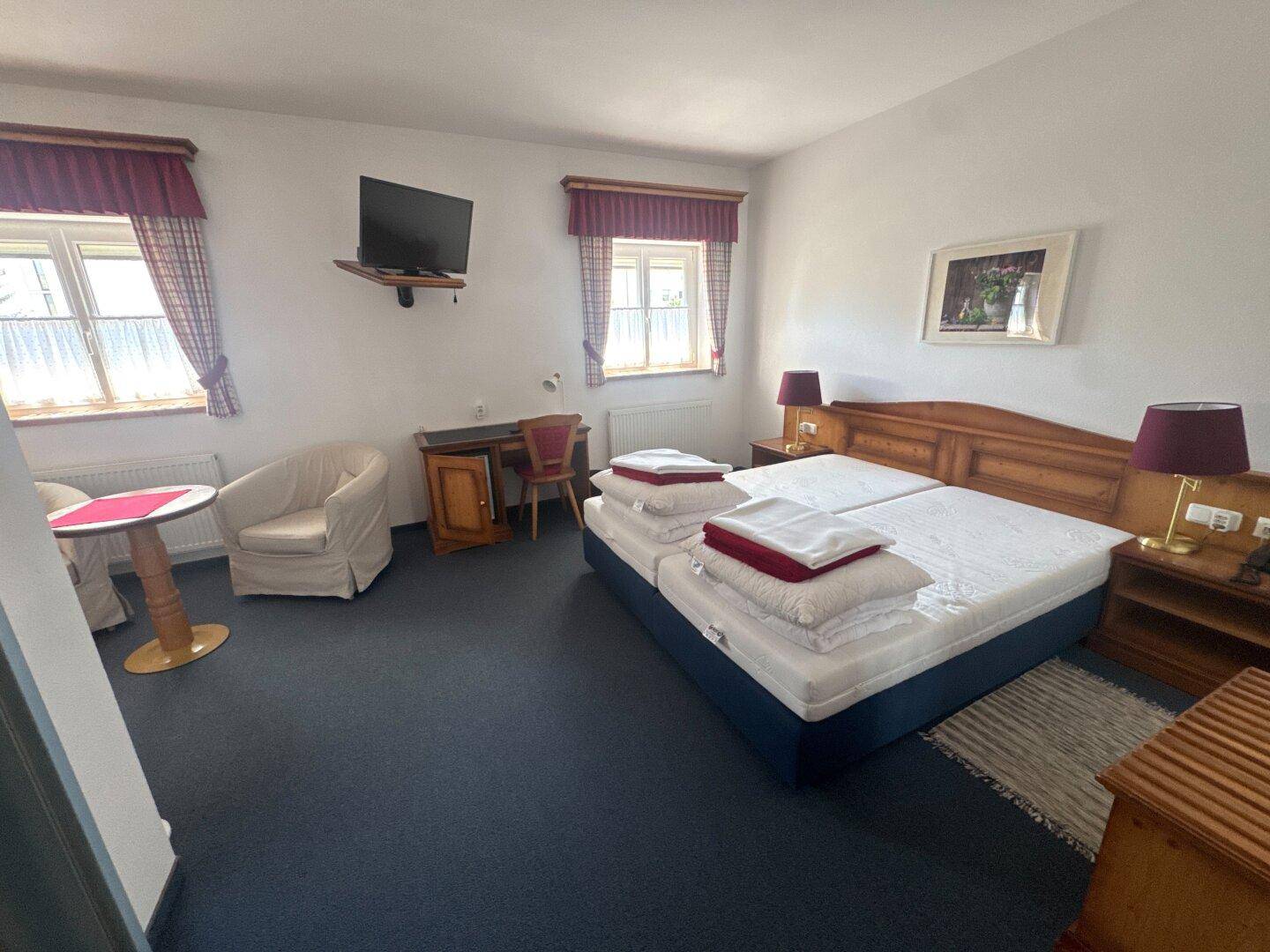 Helles Schlafzimmer mit zwei Einzelbetten, Schreibtisch und zwei Fenstern mit karierten Vorhängen.