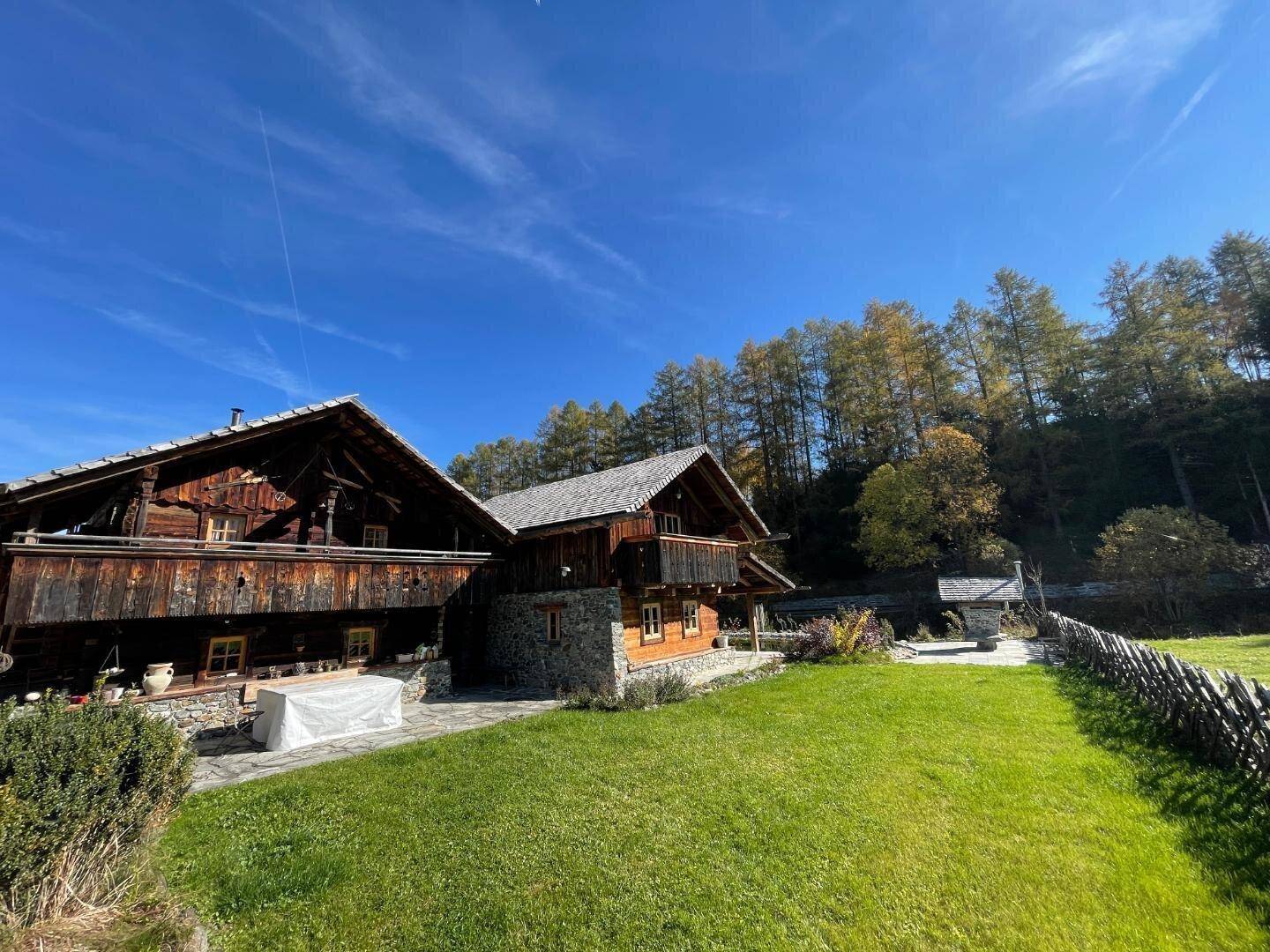Mehrere traditionelle Holzhäuser im Chalet-Stil mit weitläufigem Rasen und Wald im Hintergrund.