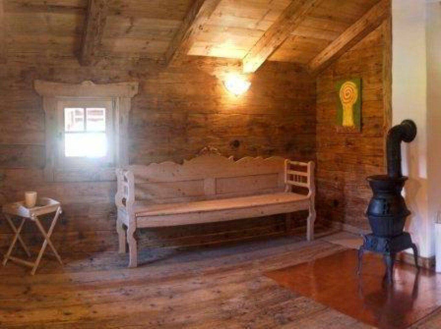Rustikaler Wohnraum mit Holztäfelung, einem gusseisernen Ofen und einer traditionellen Holzbank.