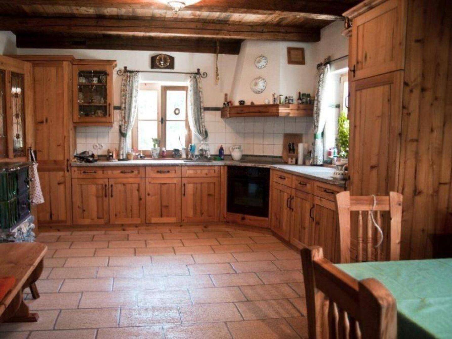 Gemütliche Landhausküche mit Holzeinbauten, Fliesenboden und traditionellem Kachelofen.