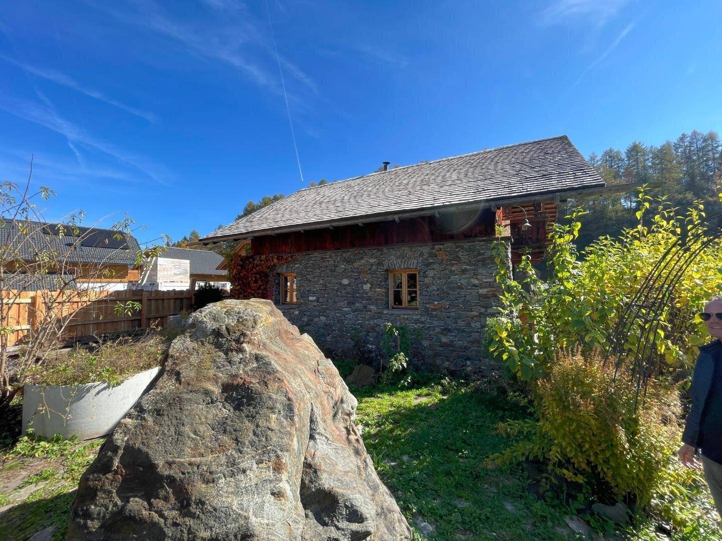 Rustikales Holzhaus mit Steinfassade und natürlicher Umgebung, umgeben von Bäumen.