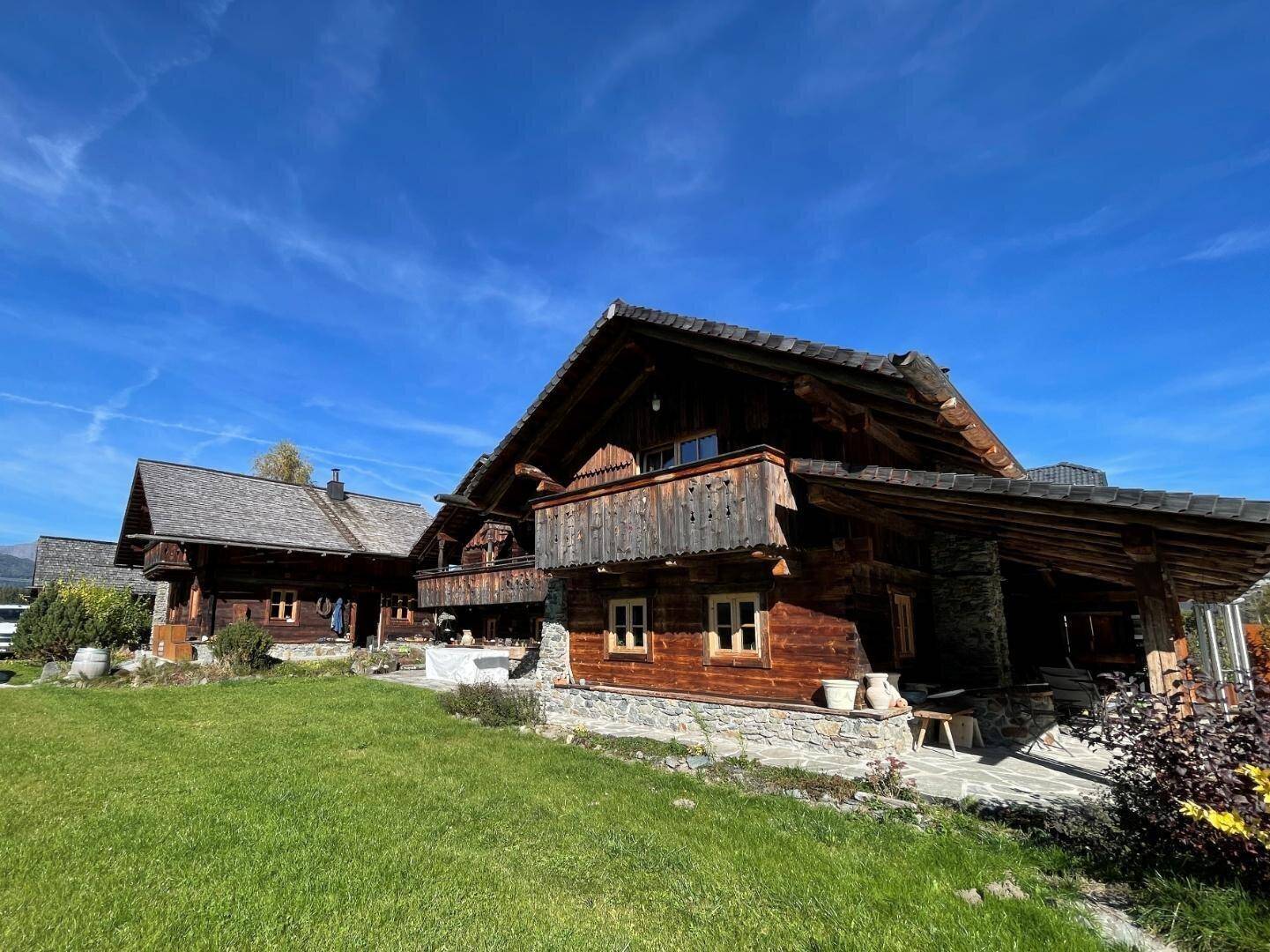 Traditionelles Holzchalet mit Steinsockel und gepflegtem Rasen unter blauem Himmel.
