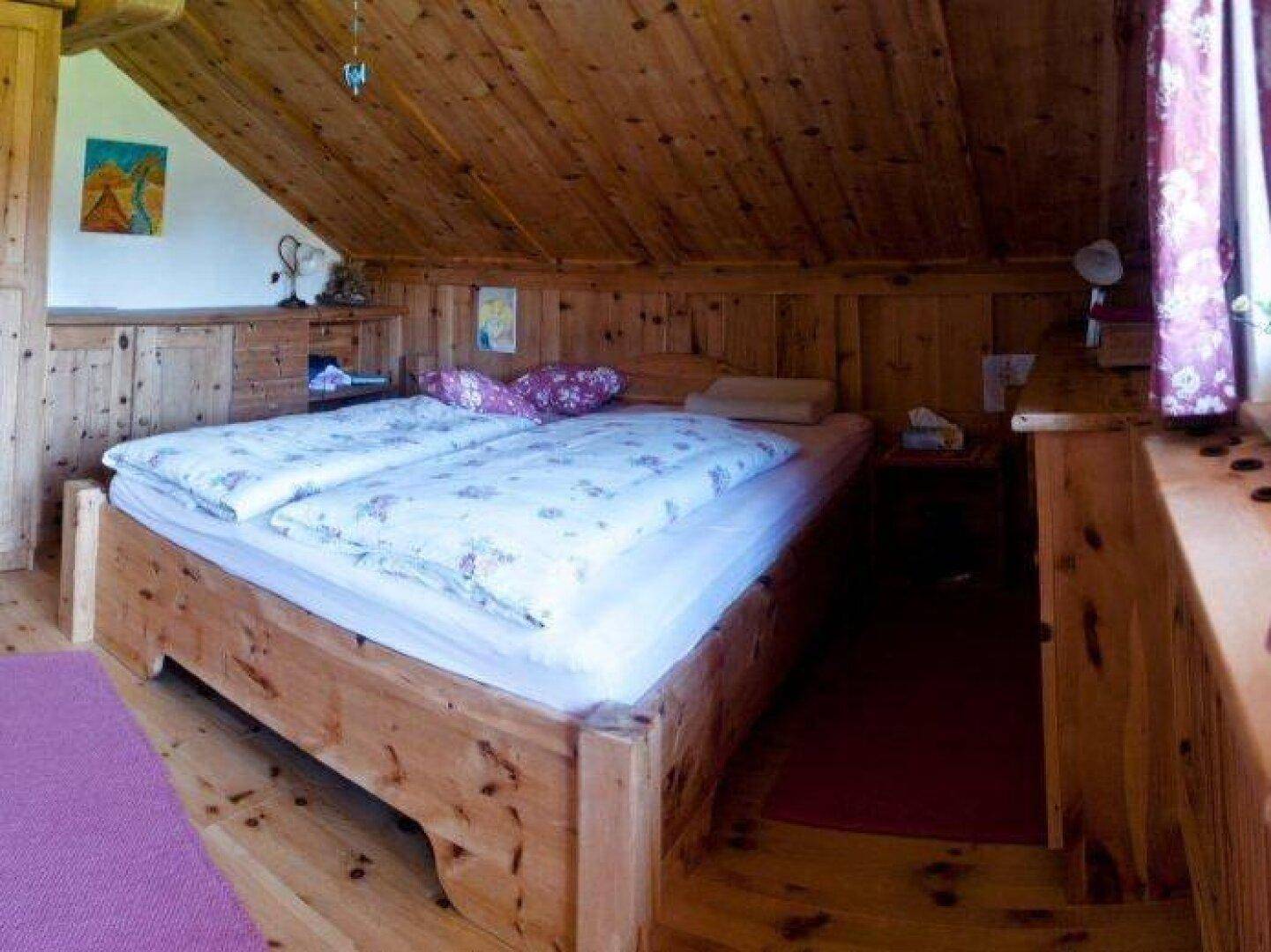 Gemütliches Schlafzimmer im Dachgeschoss mit schräger Holzdecke und rustikalem Holzbett.