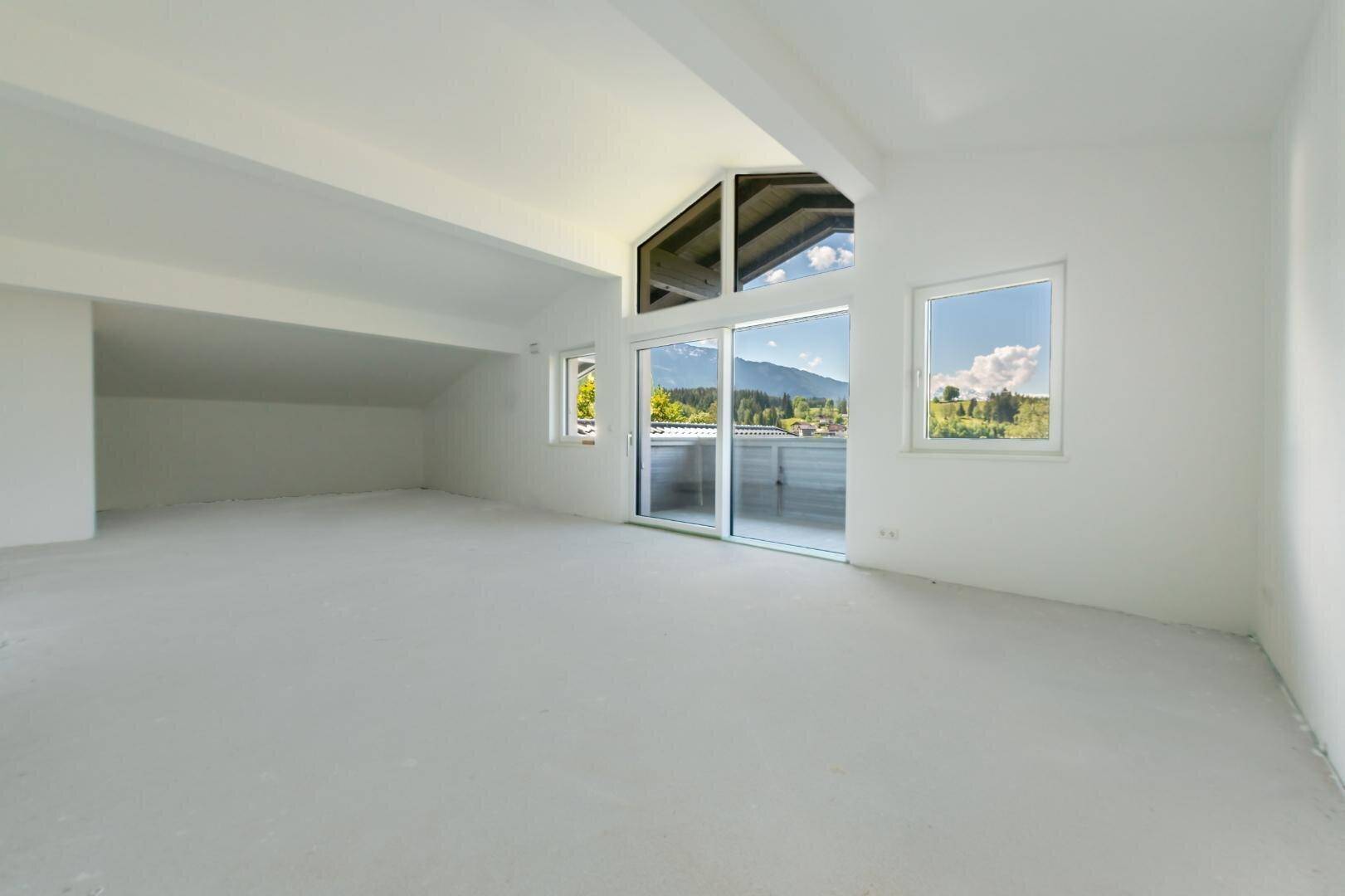 Heller, leerer Raum mit großen Fenstern und Zugang zu einem Balkon, bietet Bergblick.