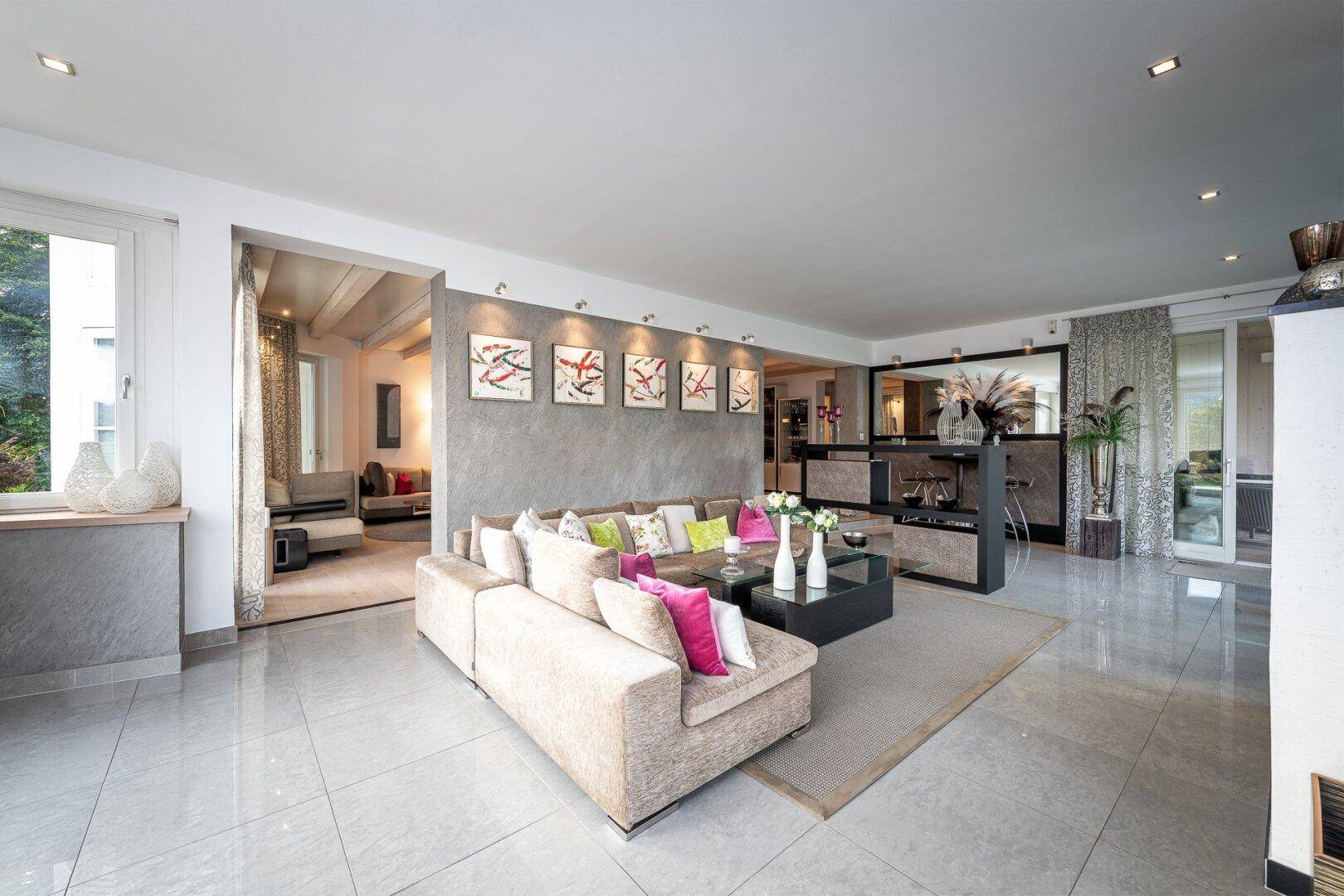 Großzügiges Wohnzimmer mit hellem Fliesenboden, beigem Sofa und moderner Dekoration.