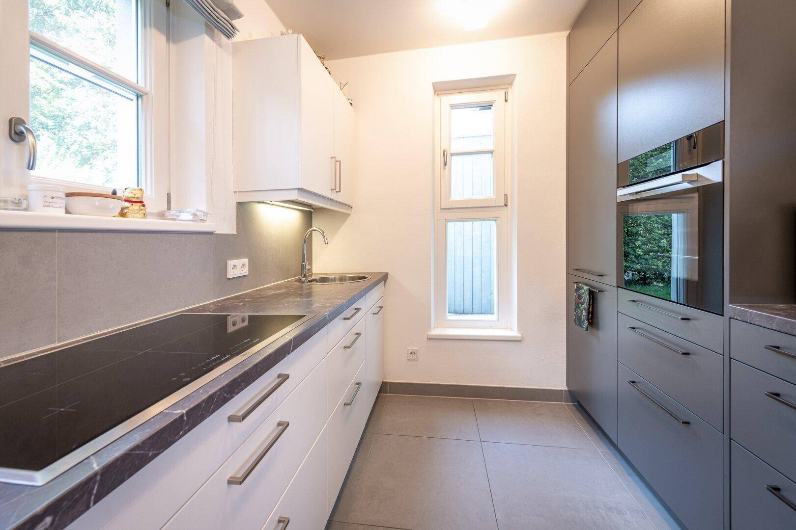 Helle, moderne Küche mit weißen und grauen Schränken, Induktionskochfeld und Fliesenboden.