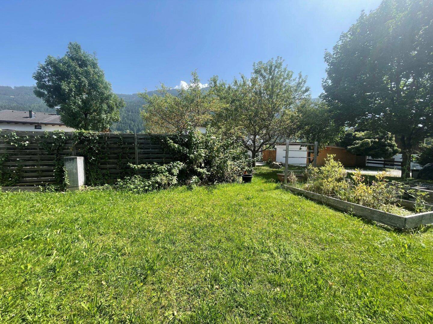 Weitläufiger Gartenbereich mit Rasen, Hochbeet, Holzzaun und Blick auf die umliegende Landschaft.