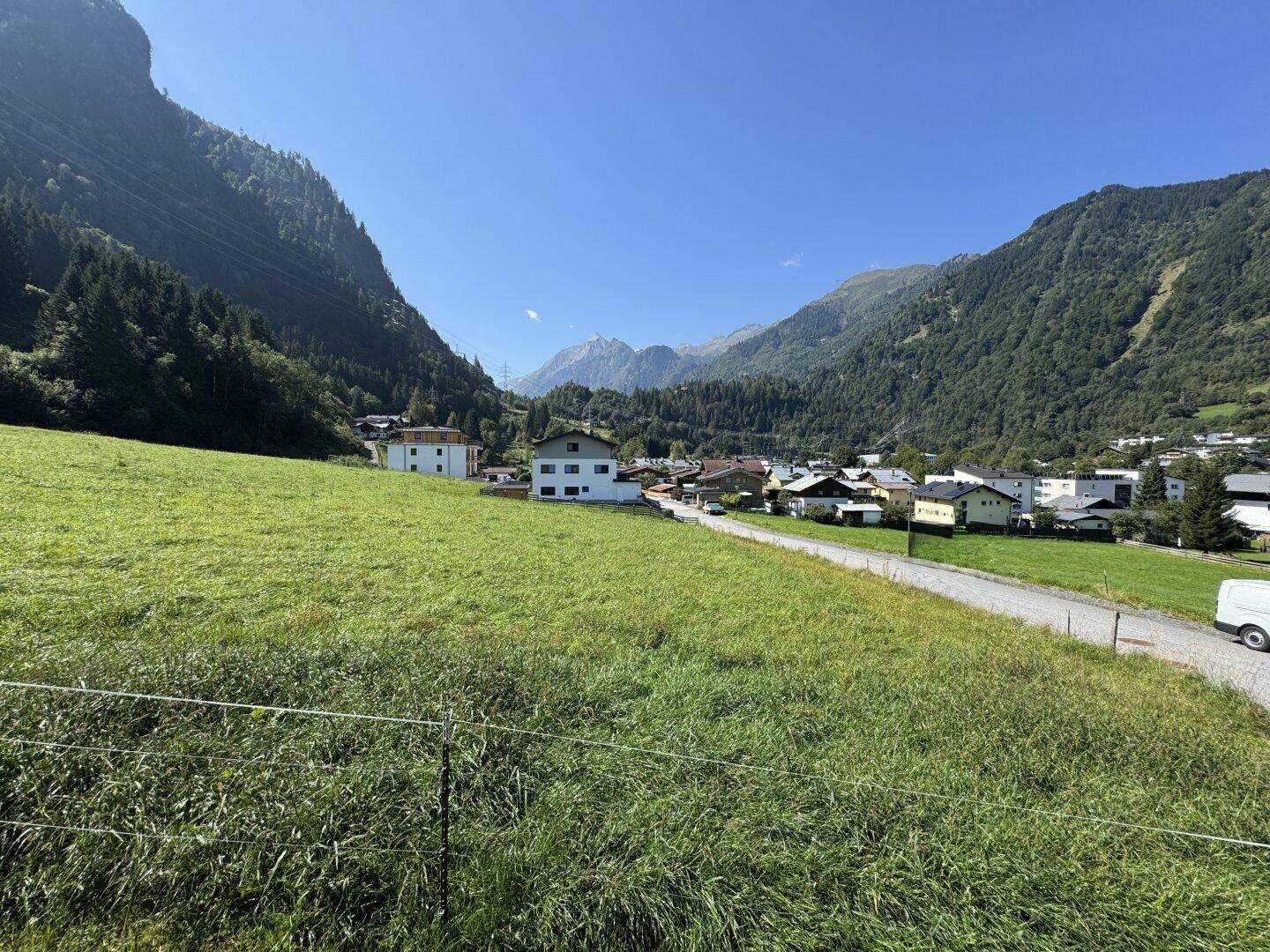 Panoramablick auf ein idyllisches Dorf, eingebettet in ein grünes Tal mit hohen Bergen und klarem Himmel.
