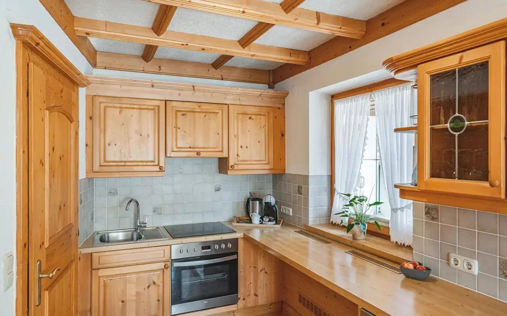 Gemütliche Küche mit hellen Holzschränken, integriertem Kochfeld und einem Fenster mit Vorhängen.