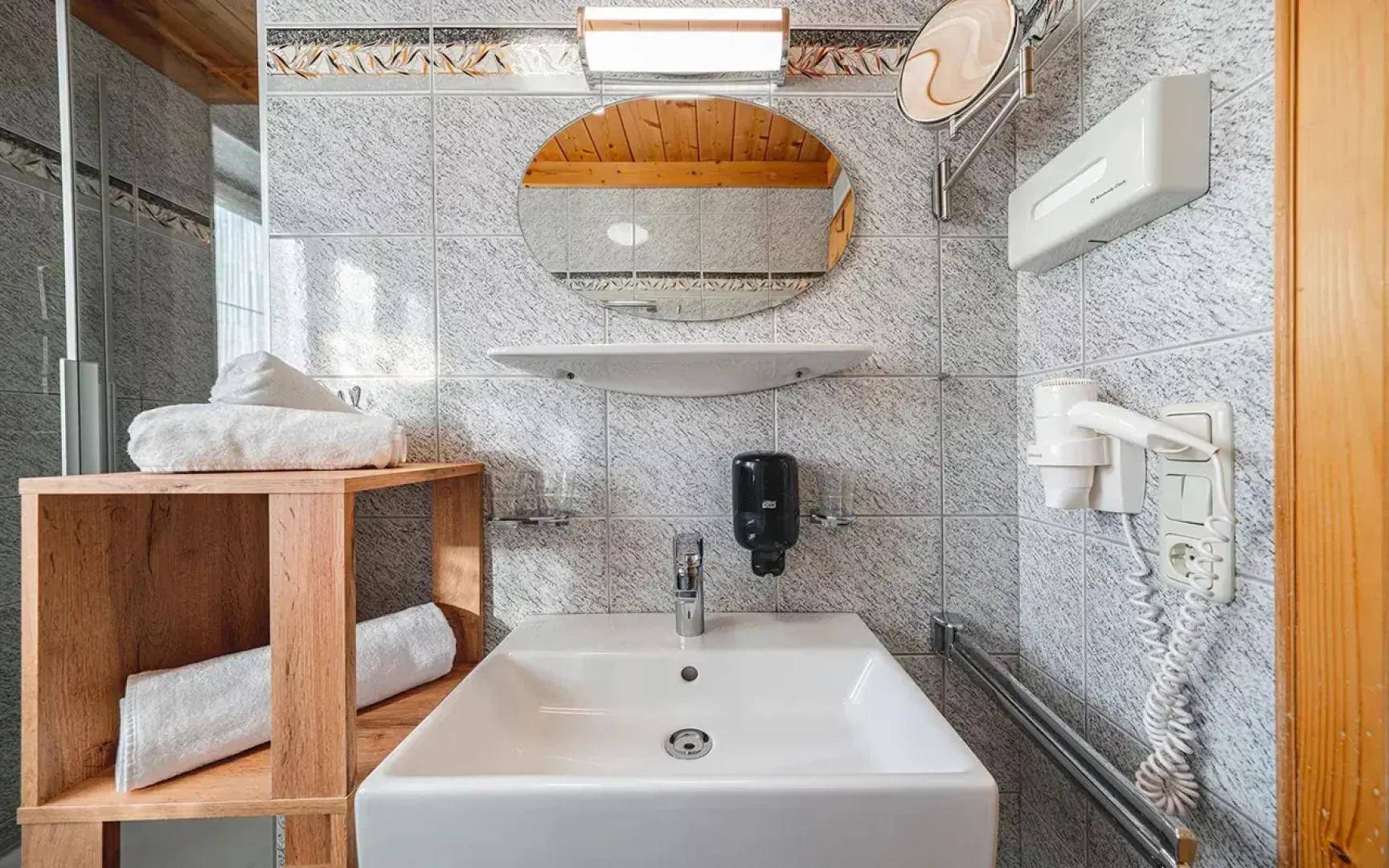 Helles Badezimmer mit modernem Waschbecken, ovalem Spiegel und hellgrauen Fliesen an den Wänden.