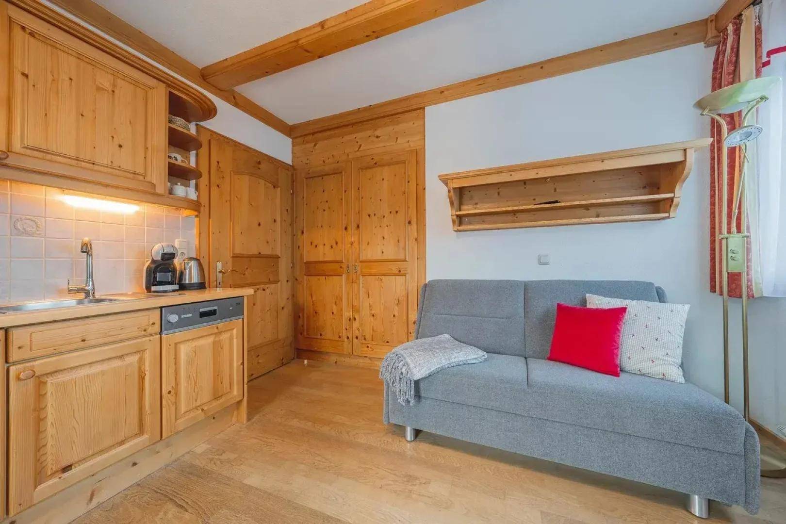 Kompakter Wohnbereich mit integrierter Küchenzeile, Sofa und Holzbalken an der Decke.