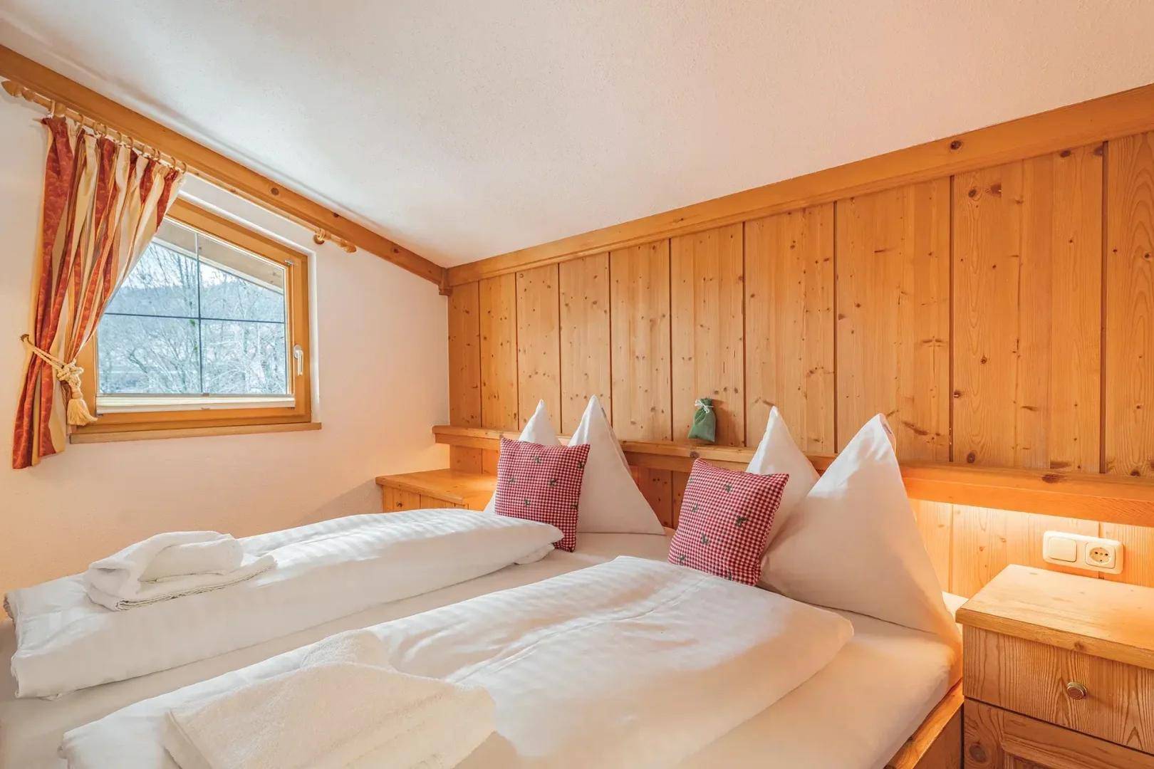 Schlafzimmer mit Doppelbett, Holzwandverkleidung und einem Fenster, das Tageslicht hereinlässt.