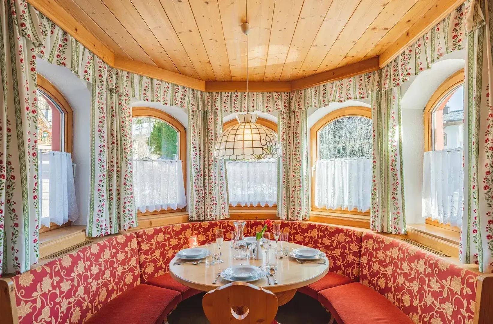 Gemütlicher Essbereich mit traditioneller Eckbank, Holztisch und mehreren Bogenfenstern.