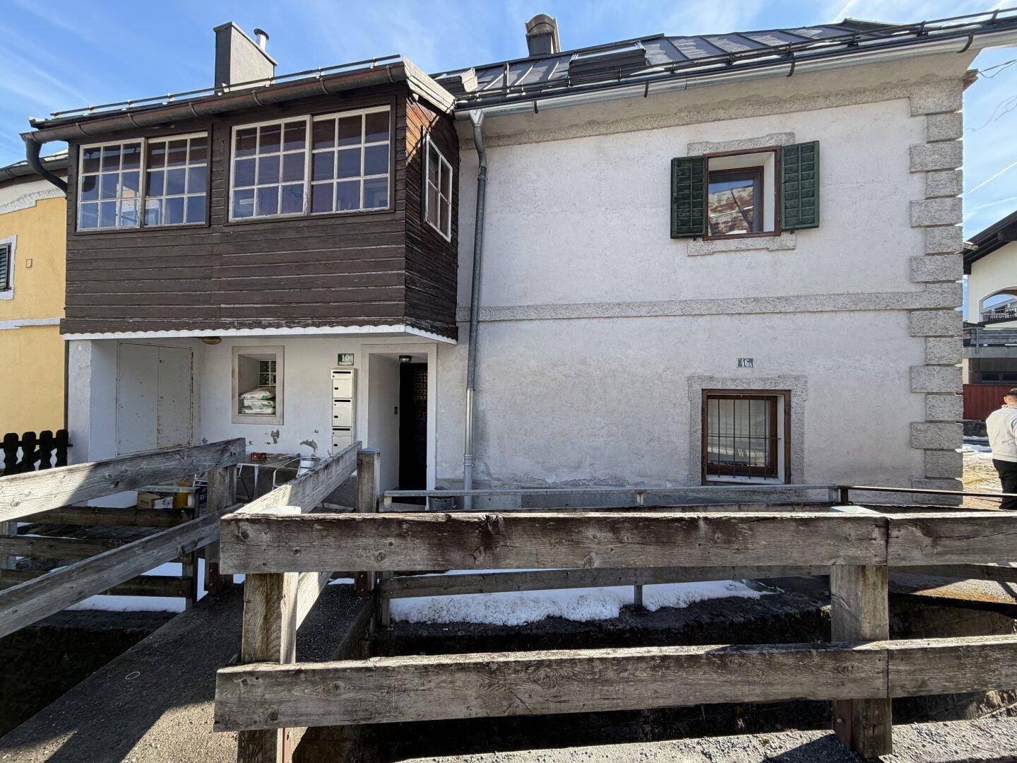 Seitenansicht des Hauses mit einer Holzrampe und traditionellen Fensterläden.