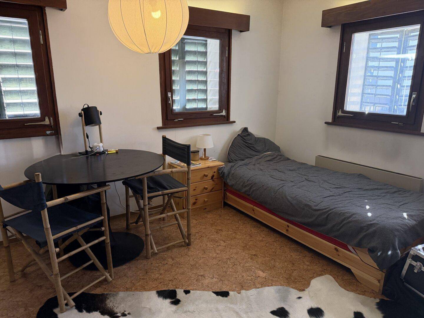 Gemütliches Schlafzimmer mit Einzelbett, kleinem Tisch und Korkboden, hell beleuchtet.
