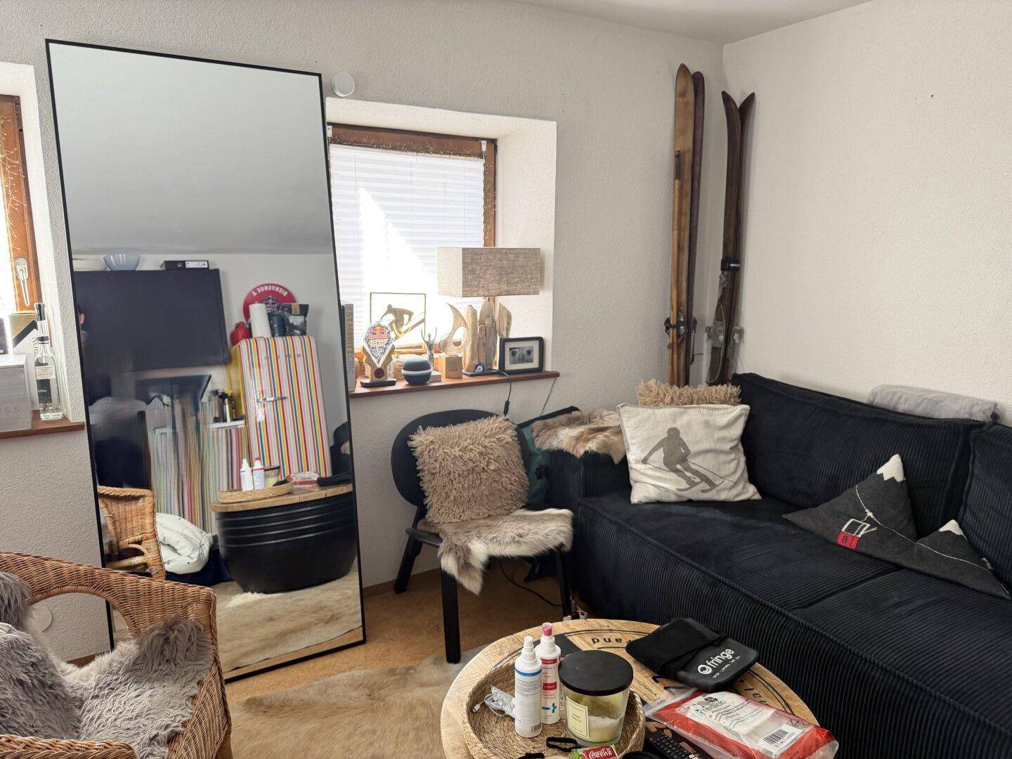 Wohnzimmer mit dunklem Sofa, großem Spiegel und rustikalen Dekorationselementen, heller Raum.