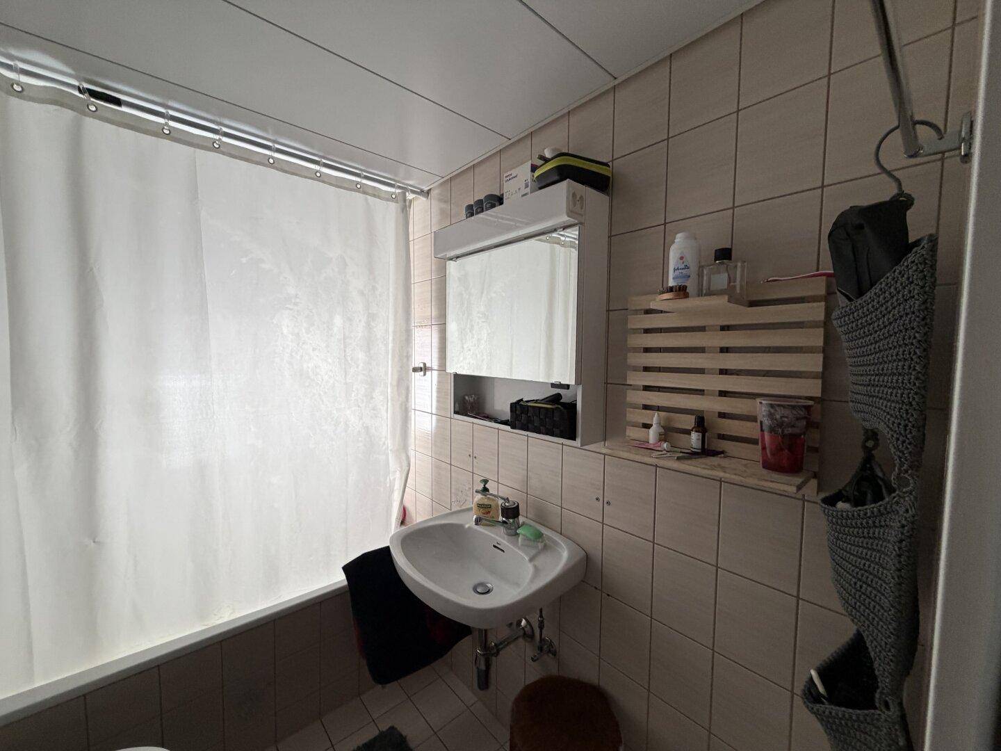 Gefliestes Badezimmer mit Badewanne, Einzelwaschbecken und Spiegelschrank.