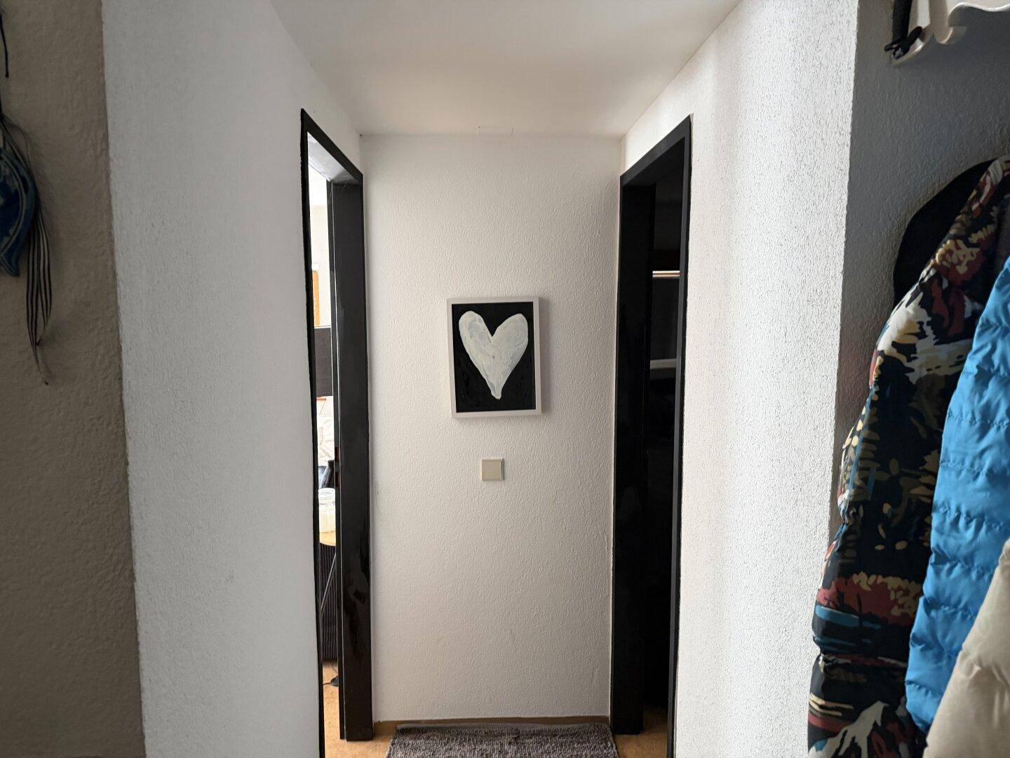 Einfacher Flur mit weißen Wänden und einem dekorativen Herzbild an der Wand.