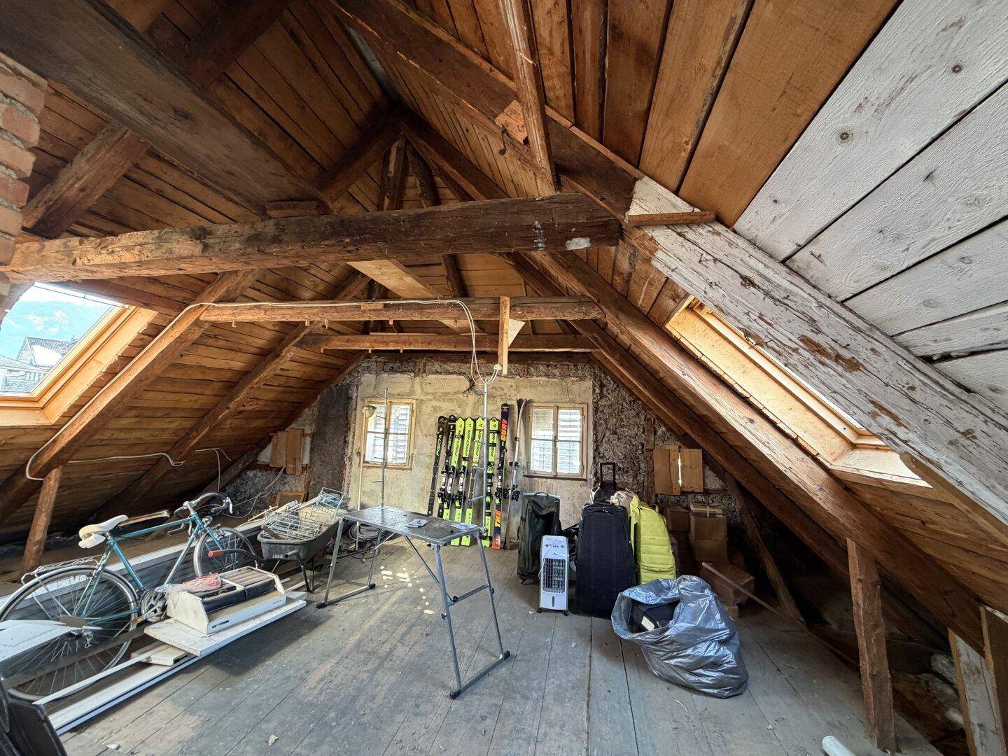Rustikaler Dachboden mit sichtbaren Holzbalken und Dachfenstern, genutzt als Abstellraum.